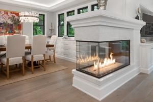 Modern dining room with white chairs and a glass corner fireplace burning in the foreground