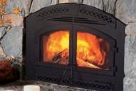 Black wood-burning fireplace insert with bright orange flames in a stone wall
