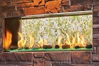 Modern stone fireplace with a long rectangular glass firebox and bright flames under a wooden mantle