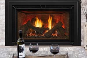Wine bottle and two glasses on a table before a lit fireplace with burning logs.
