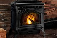 Black cast-iron fireplace stove with a visible flame on a tiled floor against a brick wall