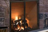 Lit fireplace with flames behind glass doors in a stone surround