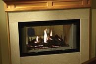 Built-in fireplace with a lit gas fire in a beige stone surround and wooden mantel