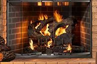 Fire burning in a brick fireplace with black logs and glowing flames