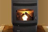 Black wood stove with a bright fire burning inside, against a tan wall.