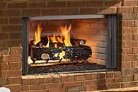 Brick fireplace with a burning log and orange flames behind a metal grate