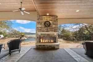 Covered patio with stone fireplace, ceiling fan, and lake view through open sides