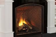 Fire burning in a brick fireplace with a black arched surround and white mantel columns
