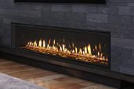 Modern linear gas fireplace with flames in a dark stone wall above hardwood flooring
