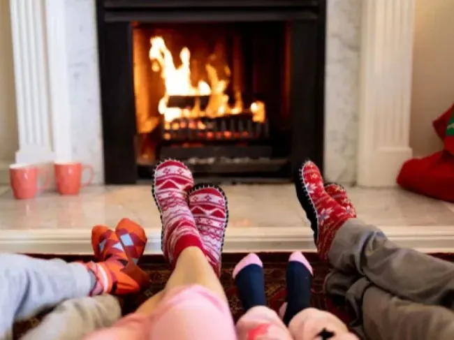 People in socks relaxing by a lit fireplace in a cozy living room