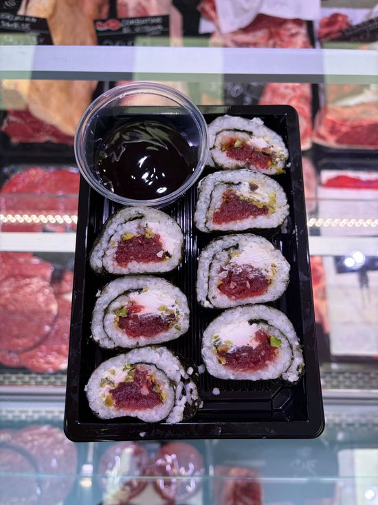 Rotoli di sushi in un vassoio nero con salsa di soia, esposti su un bancone del mercato.