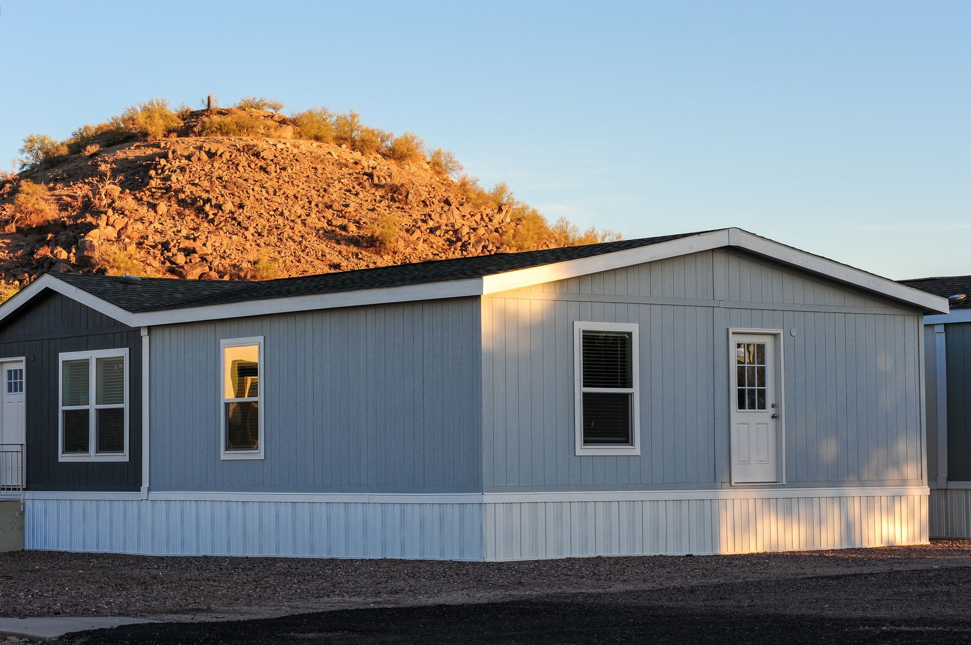 Single-wide manufactured home situated on a lot with desert hills visible in the background.