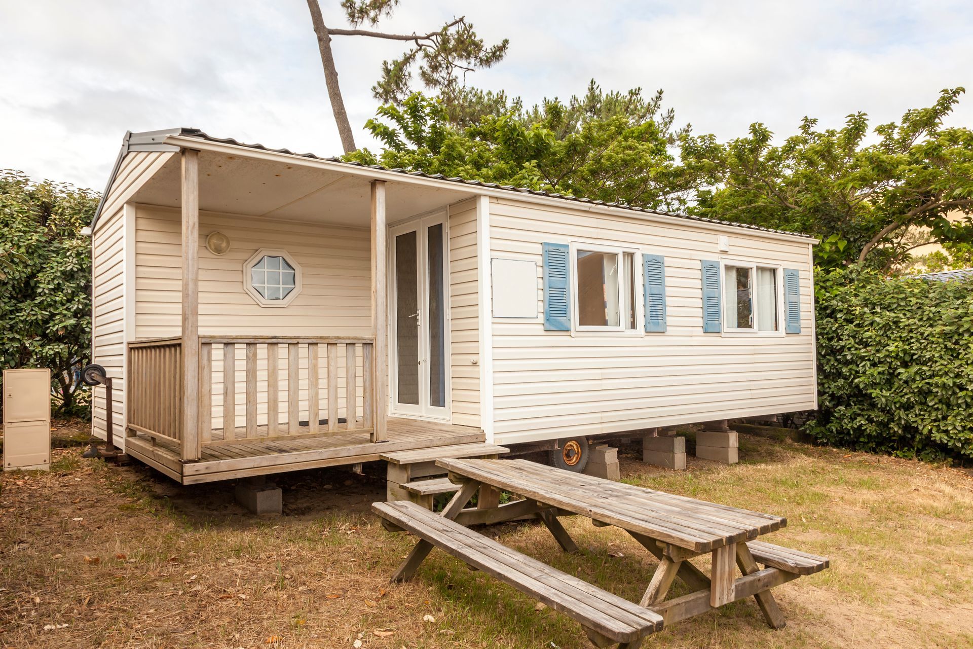 Mobile home with a small covered porch and picnic table in a landscaped outdoor setting.