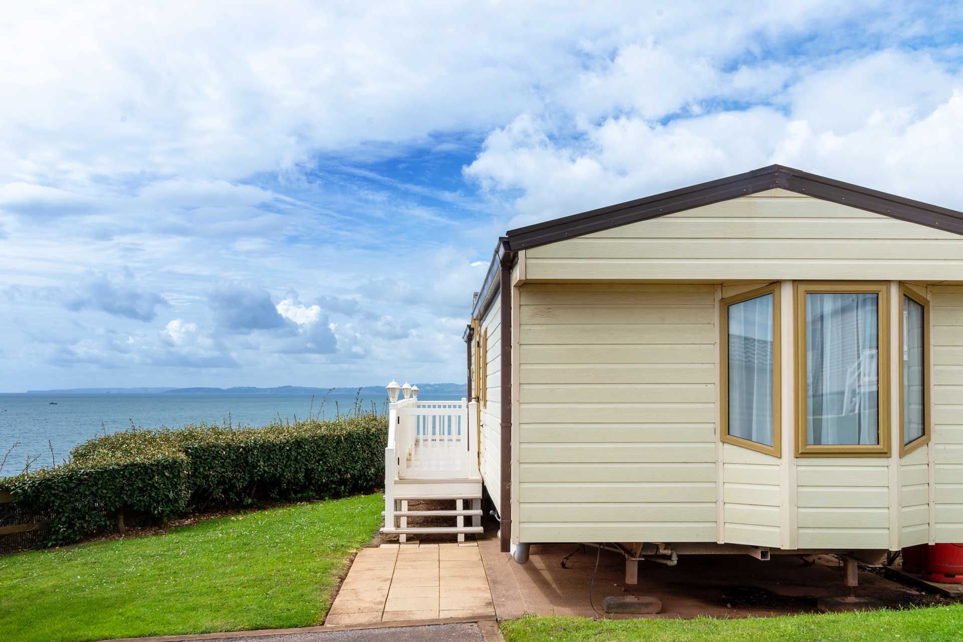 Mobile home positioned near a grassy lawn with an ocean view and a cloudy blue sky.