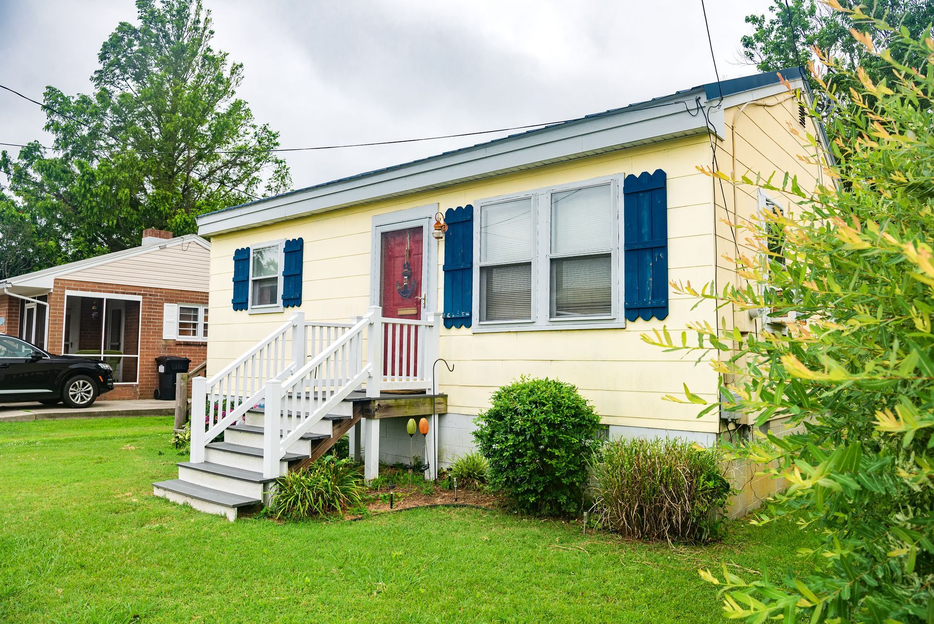 Yellow manufactured home exterior with blue shutters, red door, and siding.