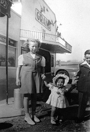 A woman and two children are standing in front of a building holding hands.