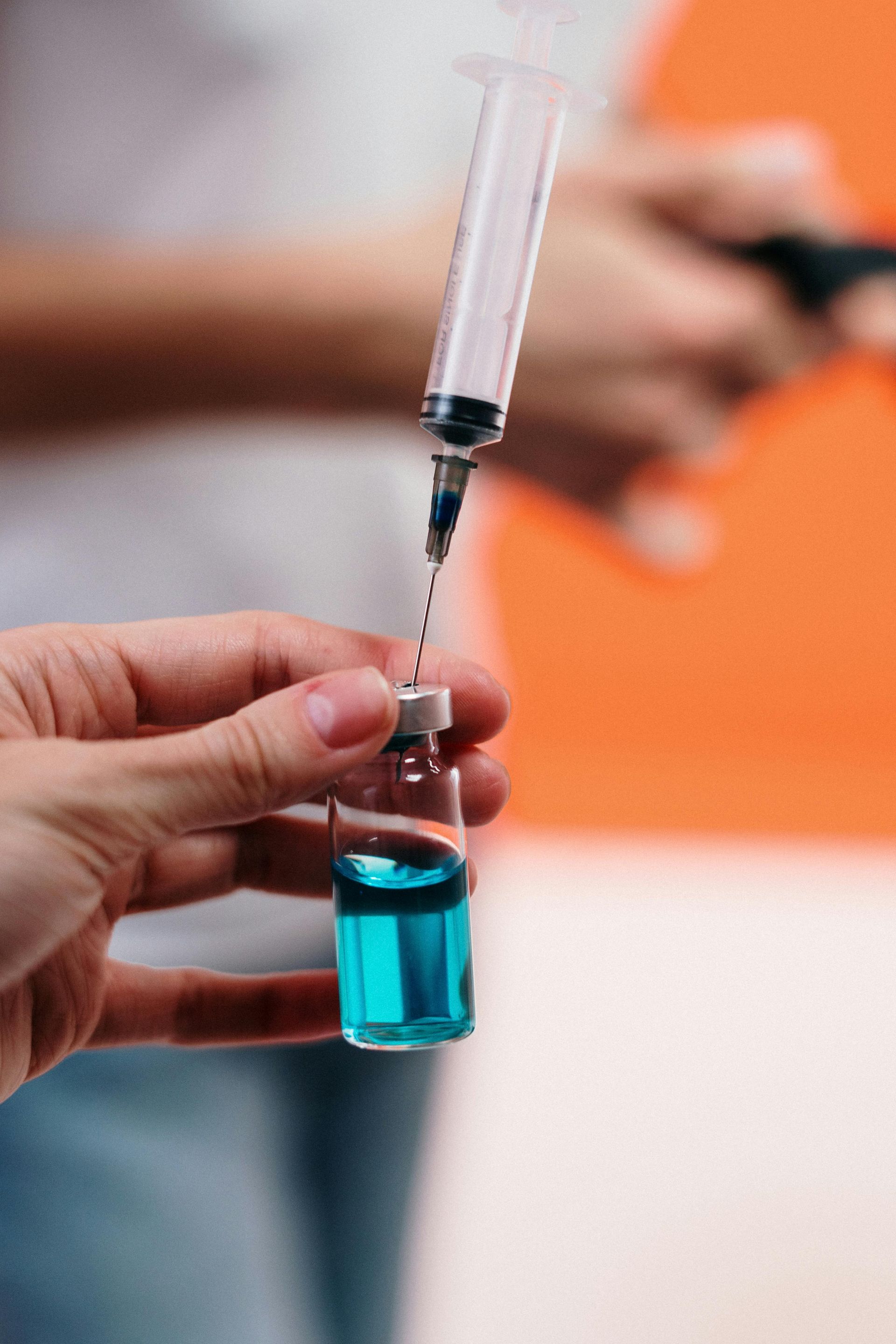 Hand holding a vial of blue liquid while drawing it into a syringe.