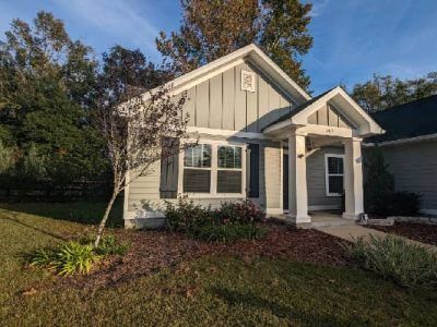 Small, light-blue house with white trim and dark shutters. Front door under a small porch. Green grass.