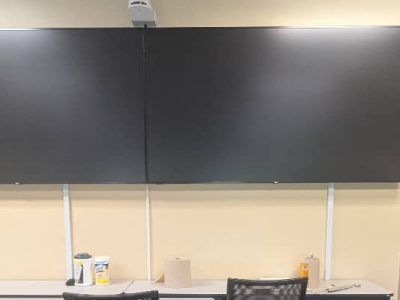 Classroom with a large, dark screen on the wall, projector above, and desks below.