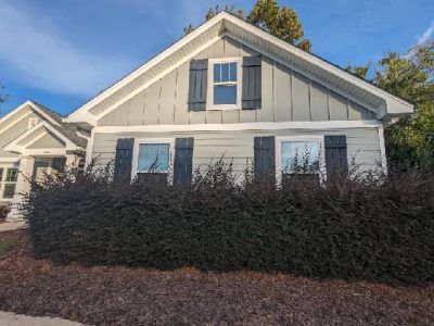 Gray house with dark blue shutters; bushes in front. Bright blue sky.
