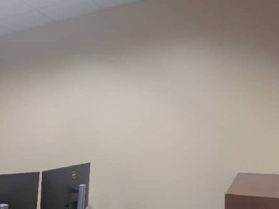 Two black computer monitors sit below a beige wall. A brown desk is on the right.