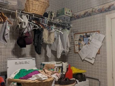 Laundry room with clothes hanging, a basket of laundry, and a cluttered shelf.