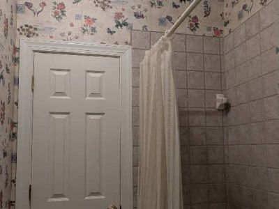 Bathroom with floral wallpaper, white door, tiled shower stall, and a shower curtain.