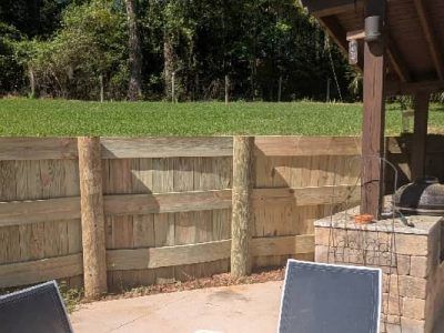 Wooden retaining wall with posts in front of a grassy yard and a stone-based structure.