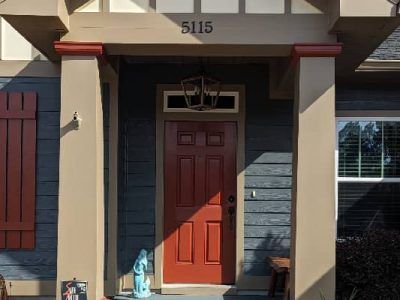 Red front door of a house with beige columns, blue siding, and red shutters. House number 5115.