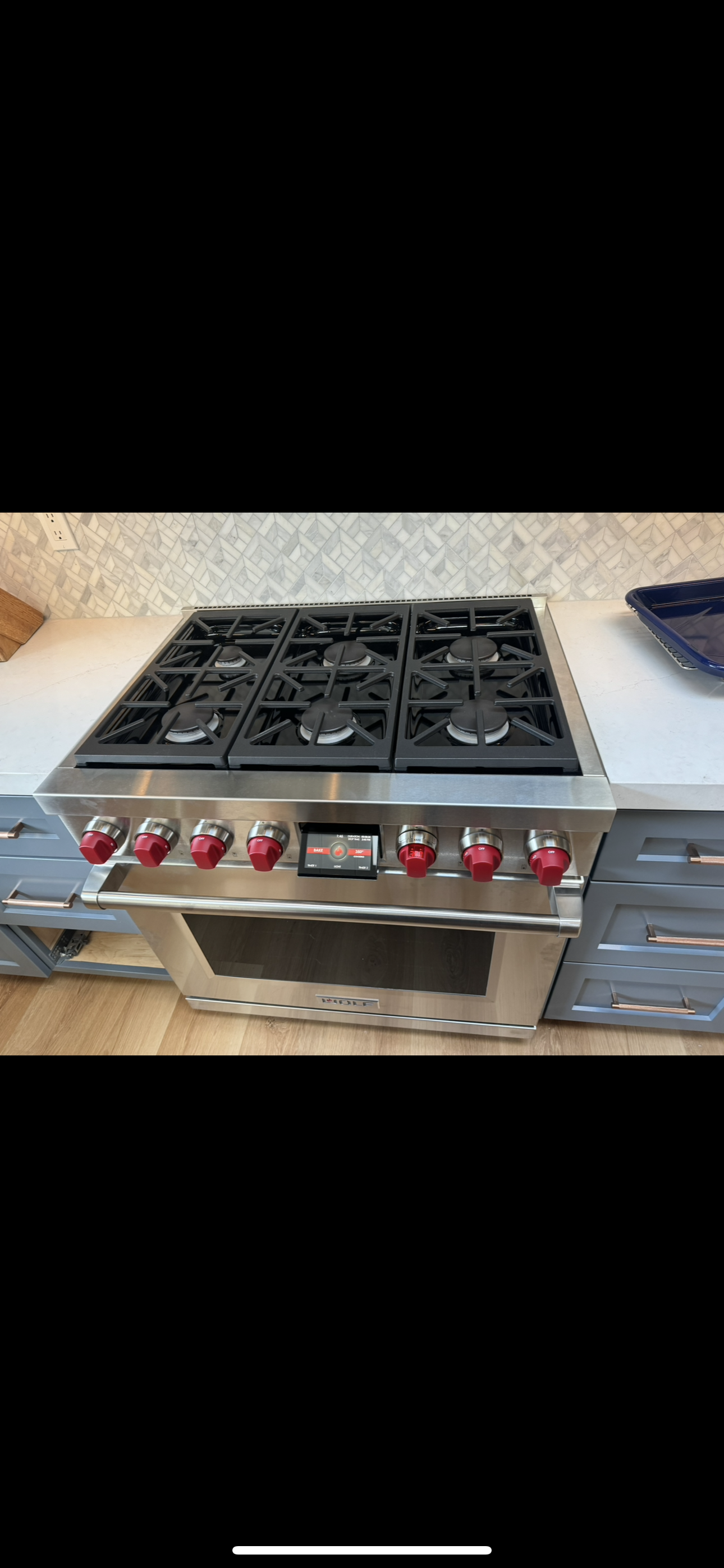 A high-end Wolf stainless steel gas range with six burners and iconic red knobs in a kitchen setting.