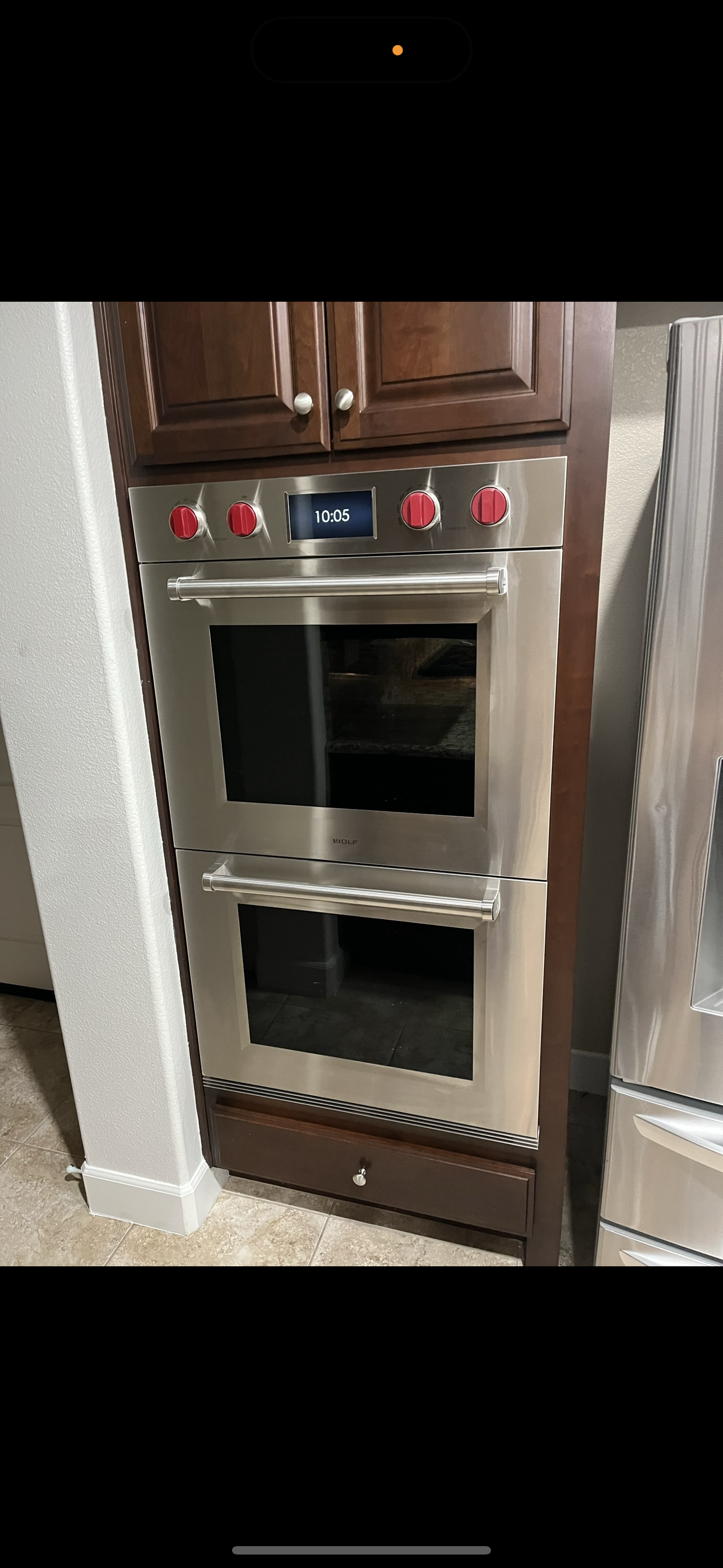 A built-in stainless steel double wall oven with signature red control knobs, installed in a dark wood kitchen cabinet.