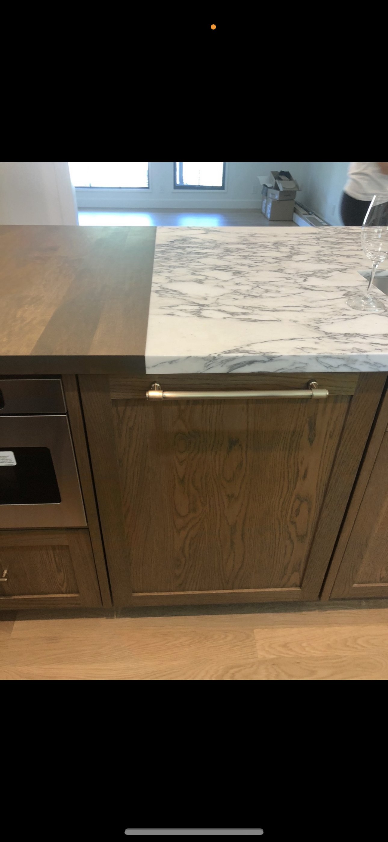A kitchen island featuring a marble countertop section transitioning to a wooden surface above cabinet-fronted appliances.