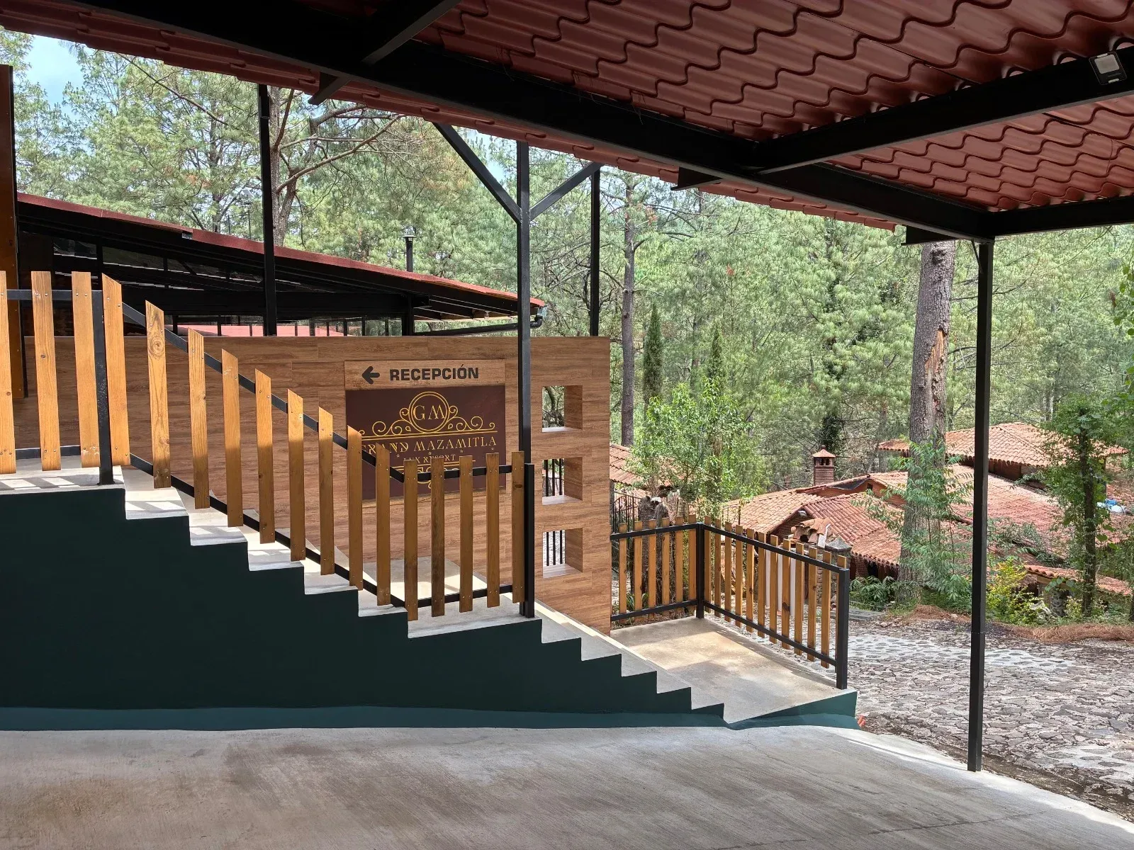 Escalera y barandilla de madera en una terraza exterior cubierta con vistas a una ladera boscosa.