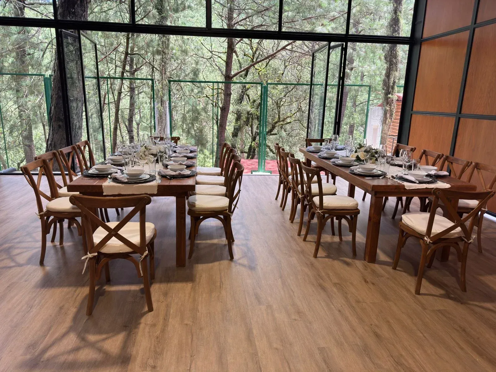 Comedor al aire libre con mesas y sillas de madera con vistas al bosque.