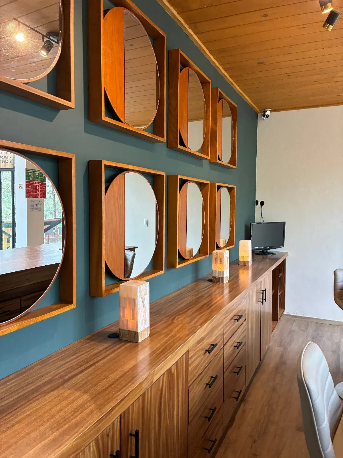 Barra revestida de madera con espejos redondos, una larga barra de madera y taburetes blancos en un interior moderno.