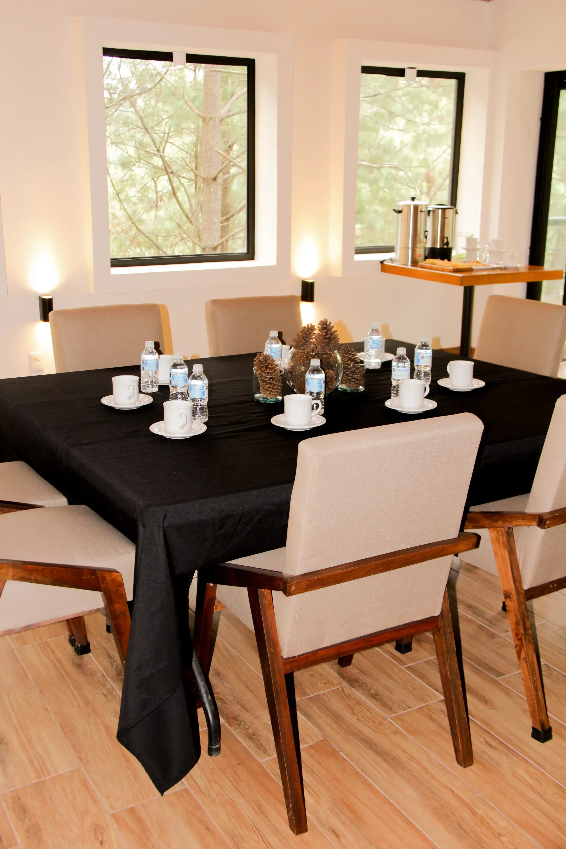 Comedor con mantel negro, sillas blancas, velas y ventanas que dejan entrar la luz natural.