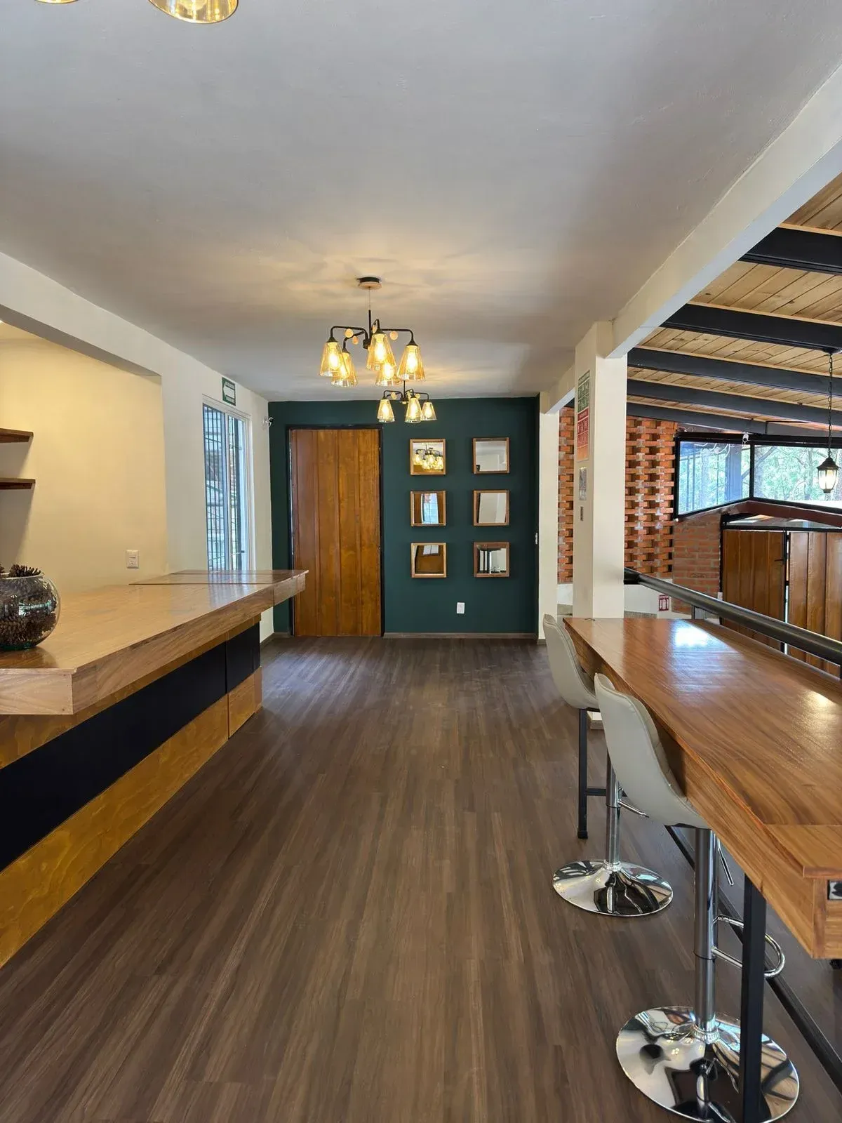 Interior de bar moderno con mostrador de madera, taburetes altos, lámparas colgantes y pared decorativa de color verde .