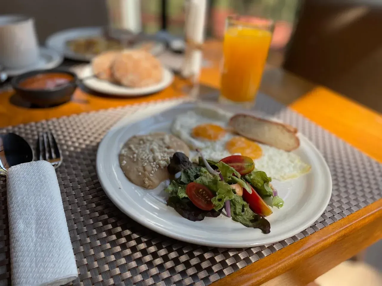 Plato de desayuno con huevos, salsa, tostadas, ensalada y zumo de naranja en una mesa de restaurante.