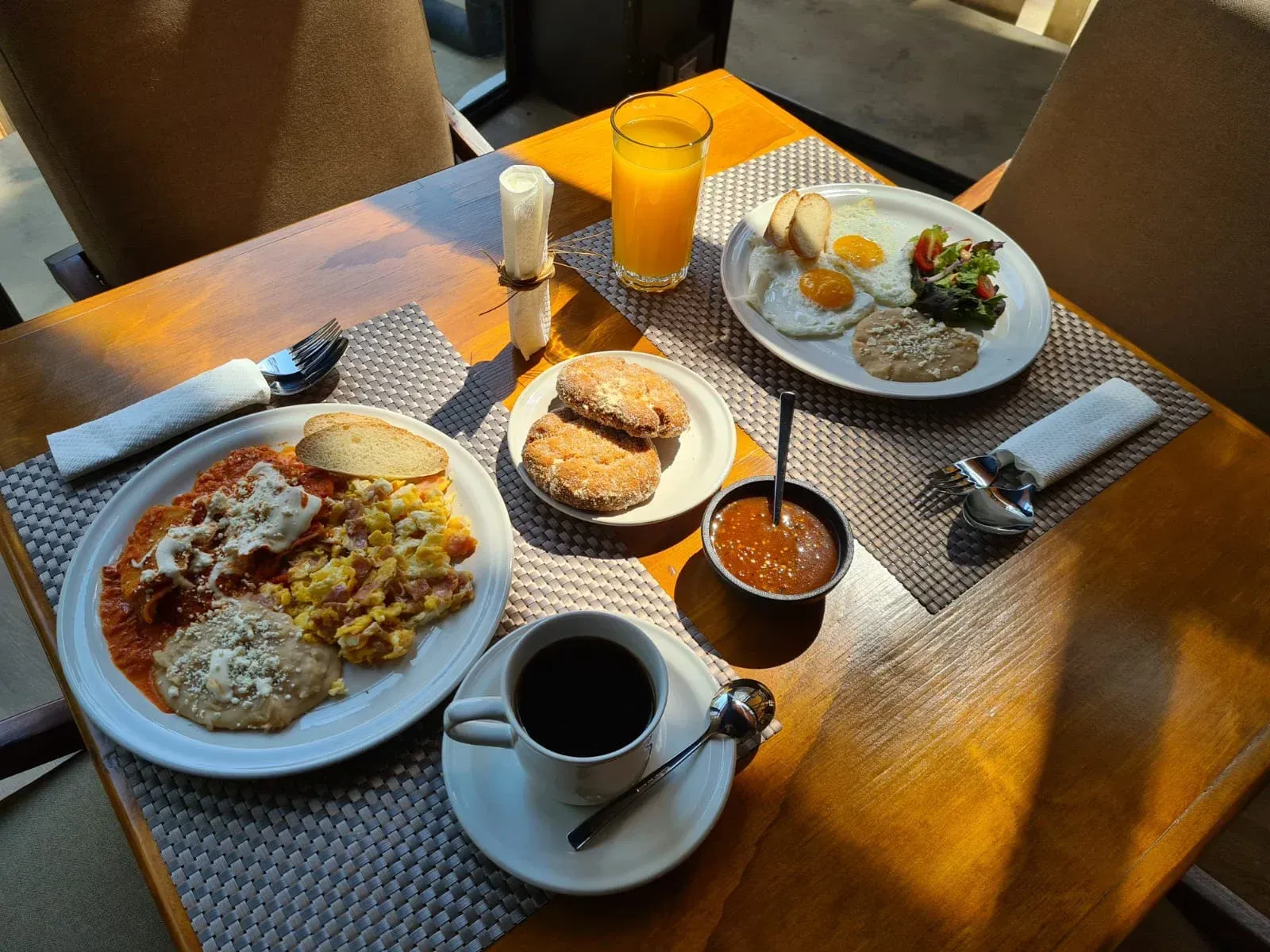 Desayuno servido en una mesa con pizza, pan, chutney, café, zumo y cubiertos.