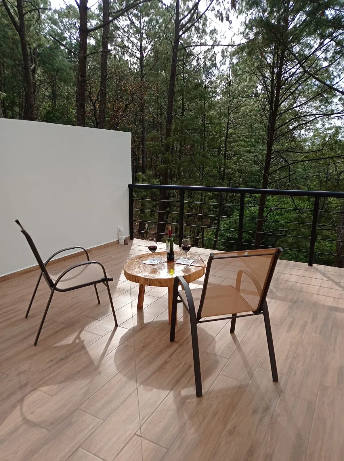Dos sillas y una mesita en una terraza de madera con vistas a los árboles y al bosque.