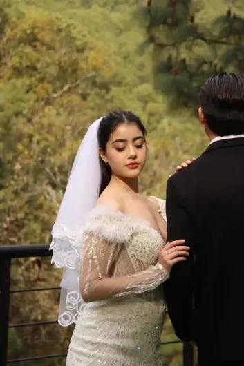 Boda en terraza hotel Mazamitla Novia con vestido blanco y velo, agarrada del brazo de un hombre, de pie junto a una barandilla con verdes colinas de fondo.