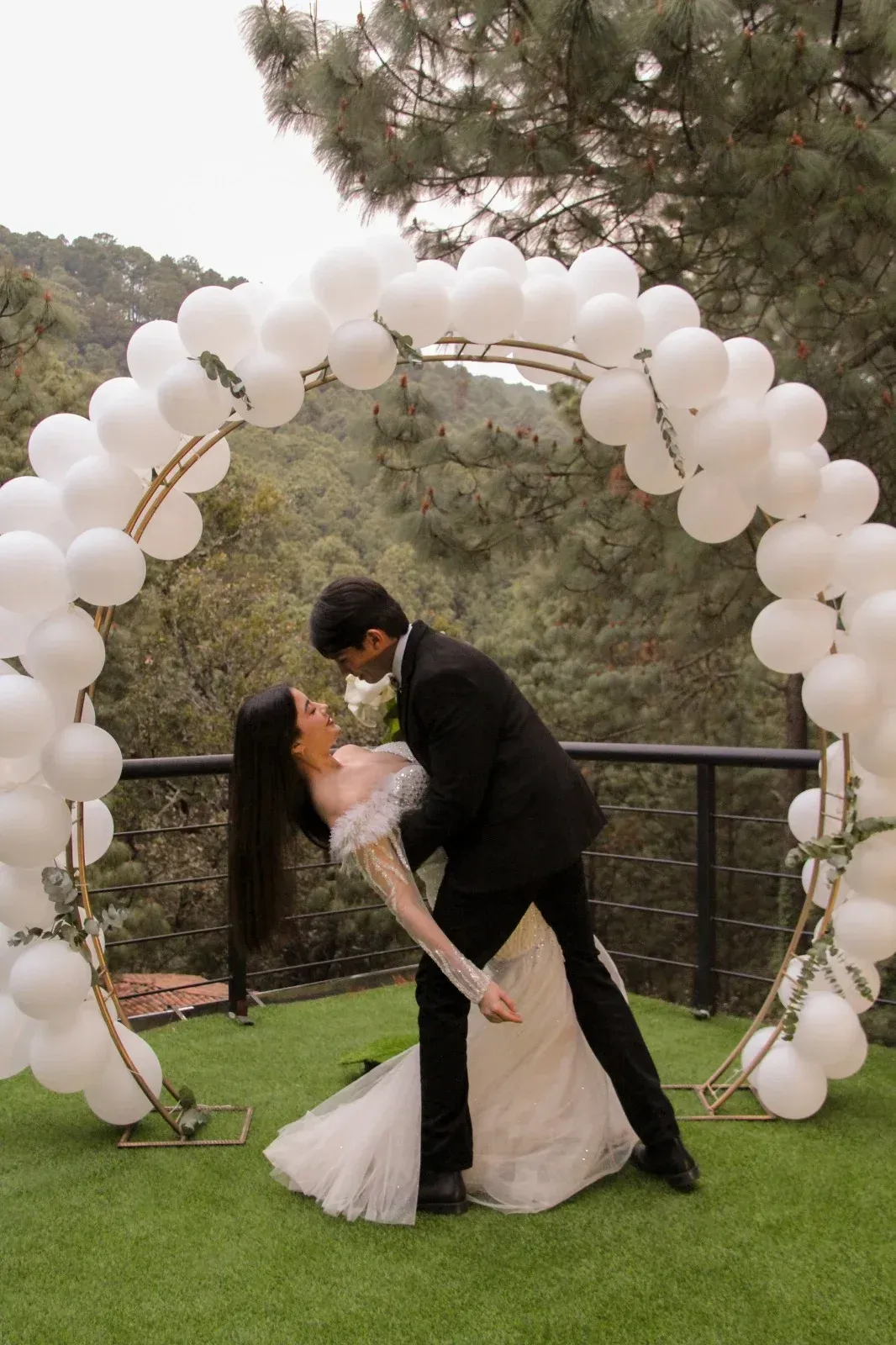Una pareja se besa bajo un arco de globos blancos en una ceremonia de boda al aire libre.