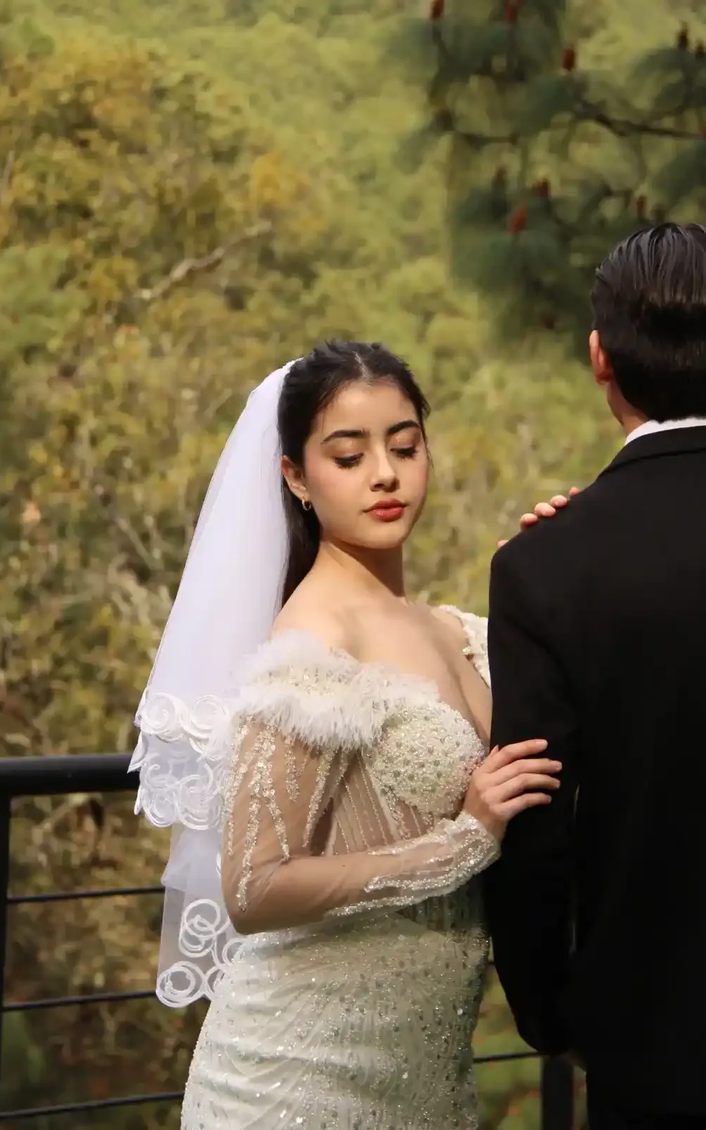 Boda en terraza hotel Mazamitla Novia con vestido blanco y velo, agarrada del brazo de un hombre, de pie junto a una barandilla con verdes colinas de fondo.