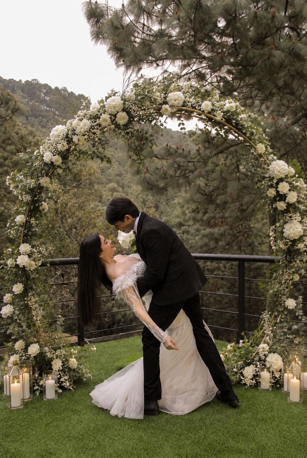Pareja de recién casados ​​besándose bajo un arco floral blanco en una ceremonia al aire libre en un jardín.