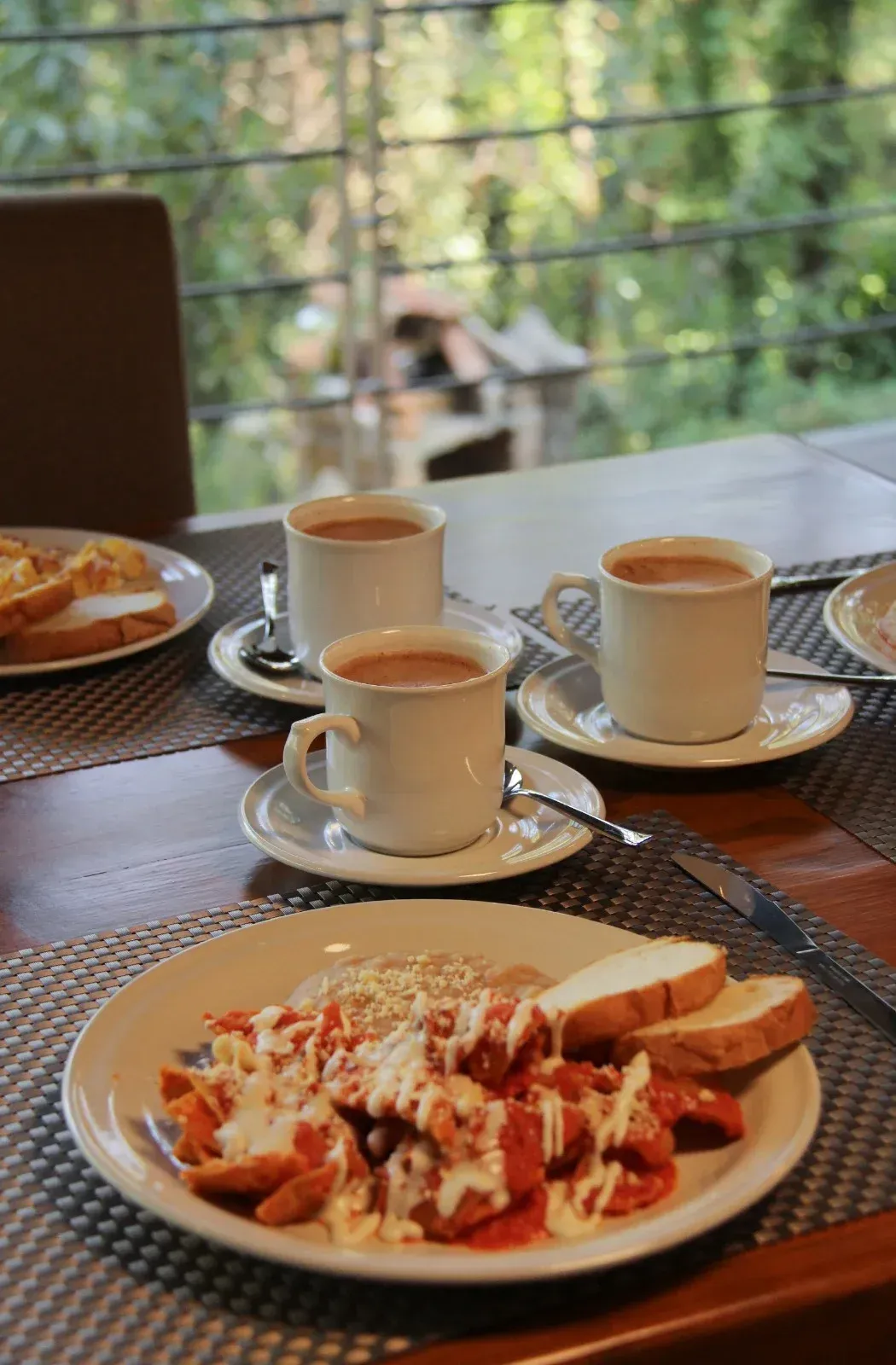 Mesa de café con tazas de café, platos de comida y una vista borrosa del patio exterior.