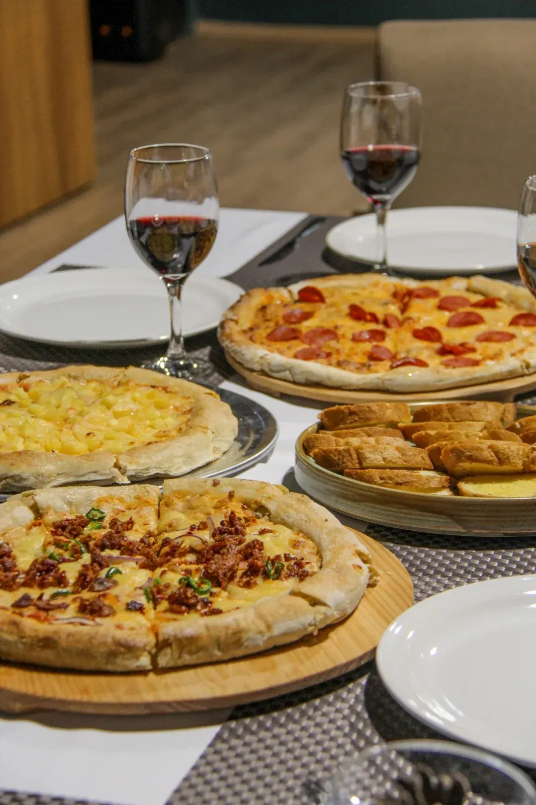 Mesa con varias pizzas y copas de vino tinto en un ambiente de restaurante.
