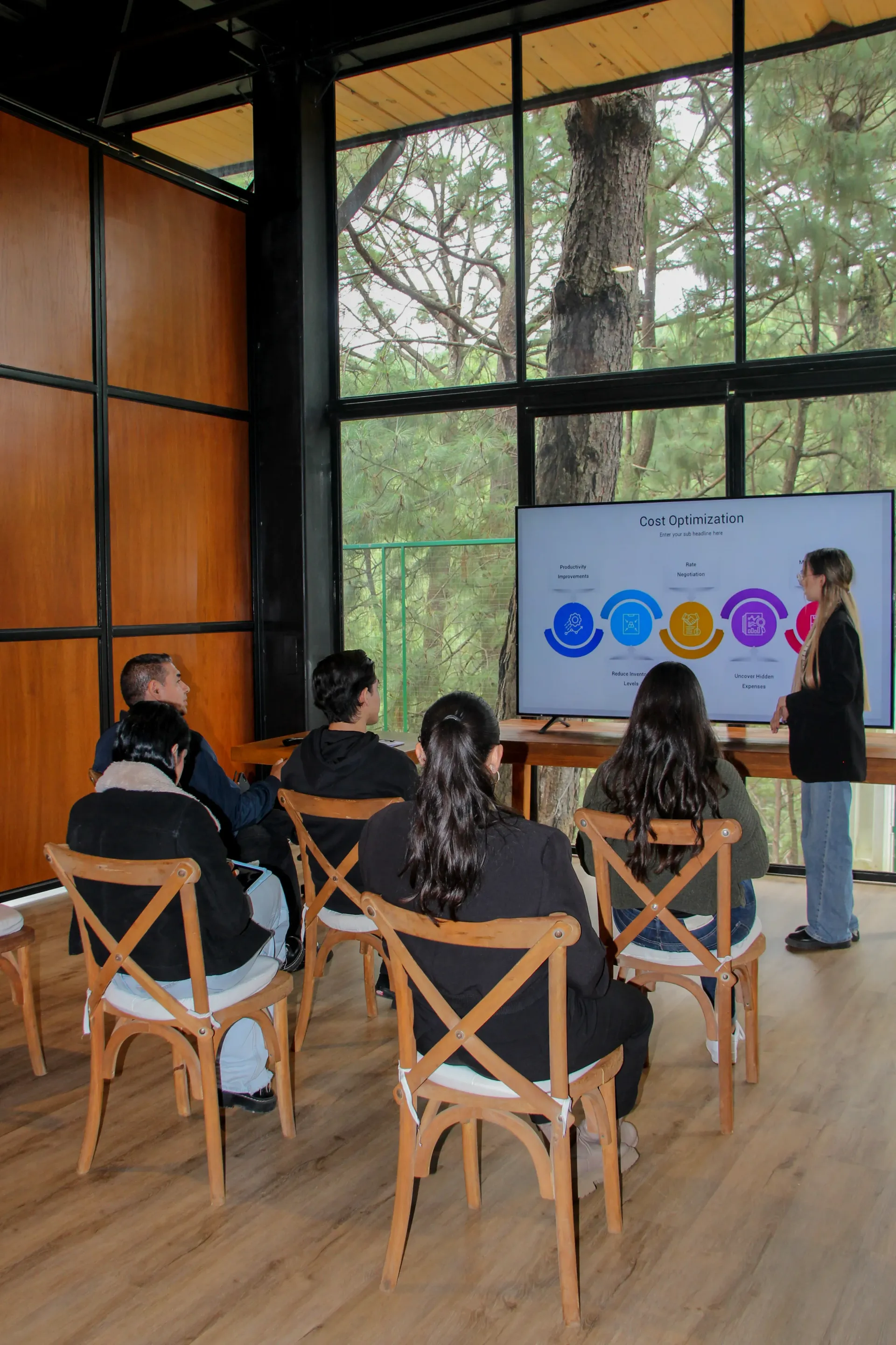 Personas sentadas en una moderna sala de reuniones viendo una presentación en una pantalla.