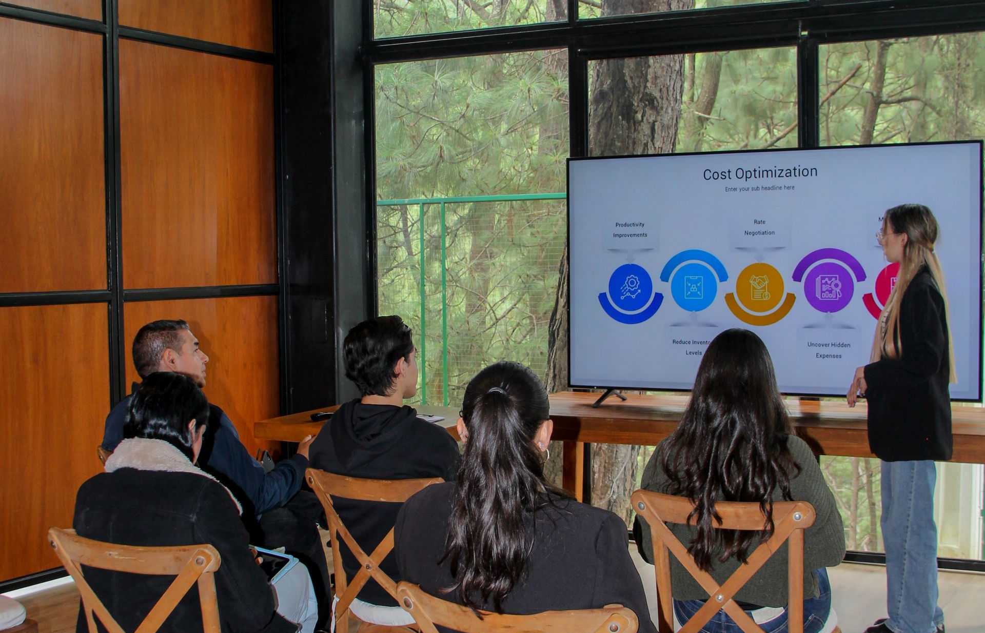 Personas sentadas en una moderna sala de reuniones observan a un presentador junto a una pantalla con coloridos gráficos