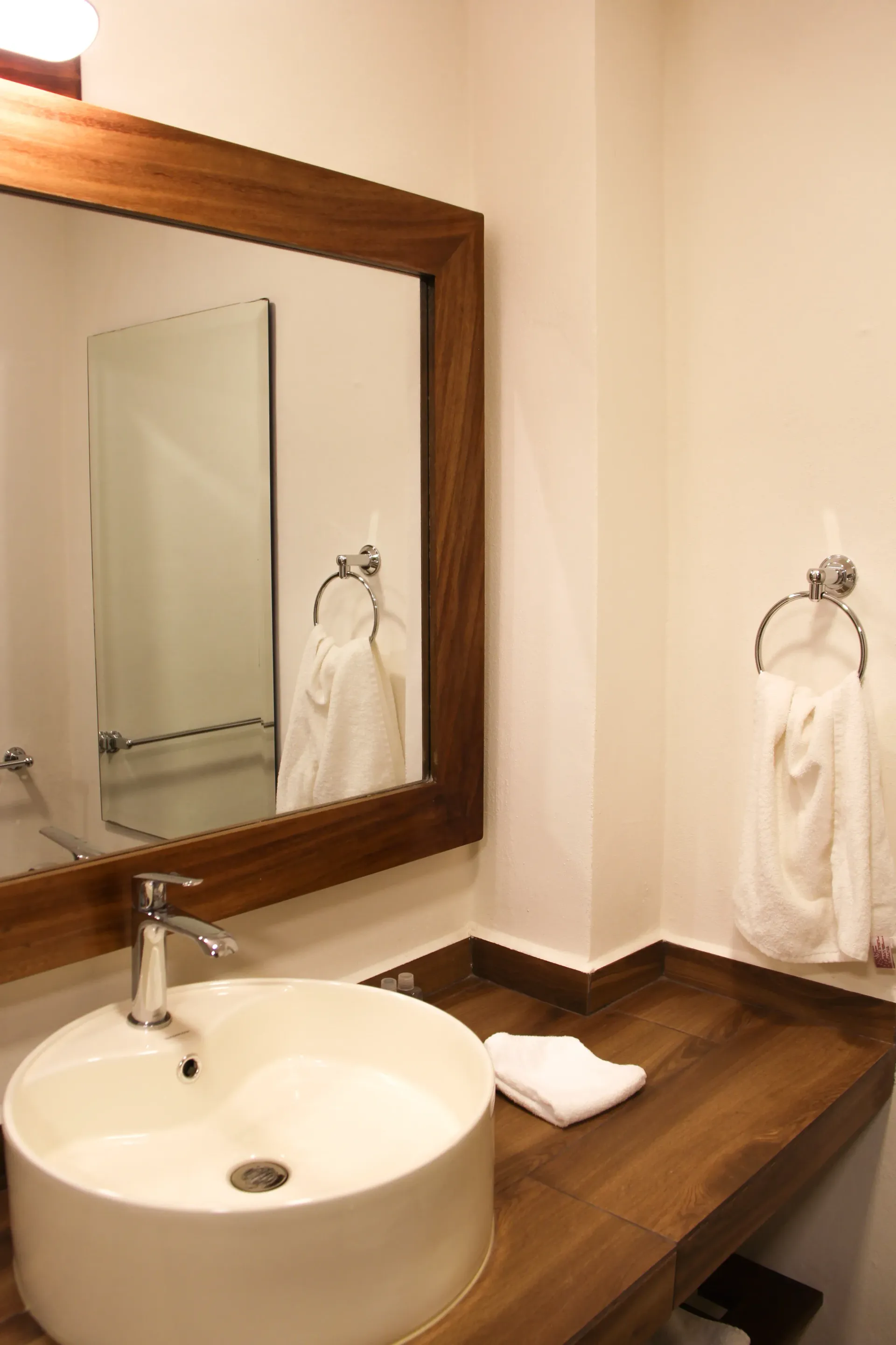 Mueble de baño con lavabo redondo, espejo grande, aro para toallas y encimera de madera.
