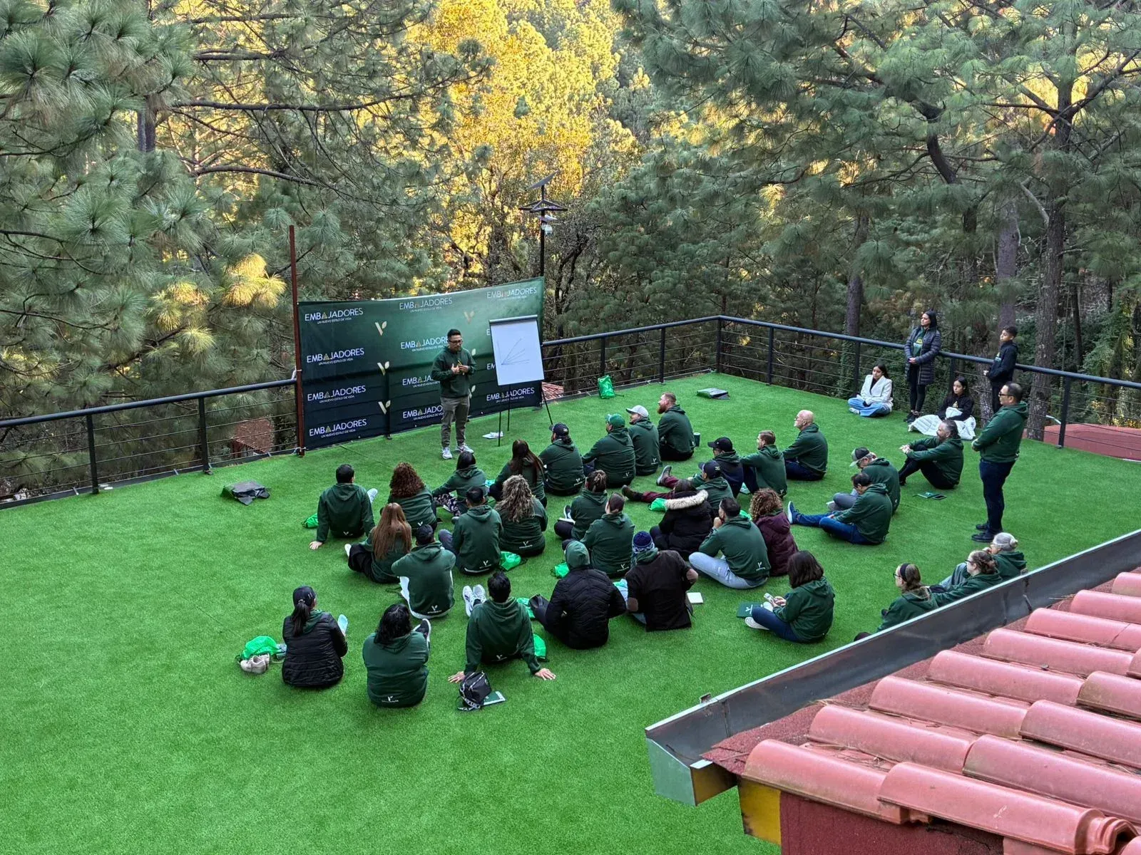Los alumnos estaban sentados al aire libre sobre el césped para una clase grupal, con una pizarra y árboles otoñales cerca.